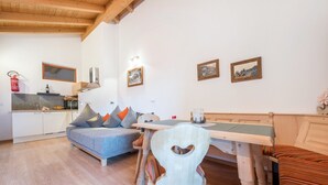 Een gezellige kamer met een houten plafond, een bank, een eettafel met stoelen, en een keukenhoek met een brandblusser.