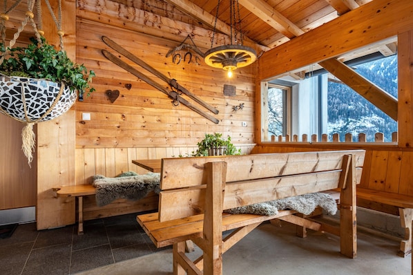 A wooden cabin interior with a bench, hanging plants, and a rustic light fixture.
