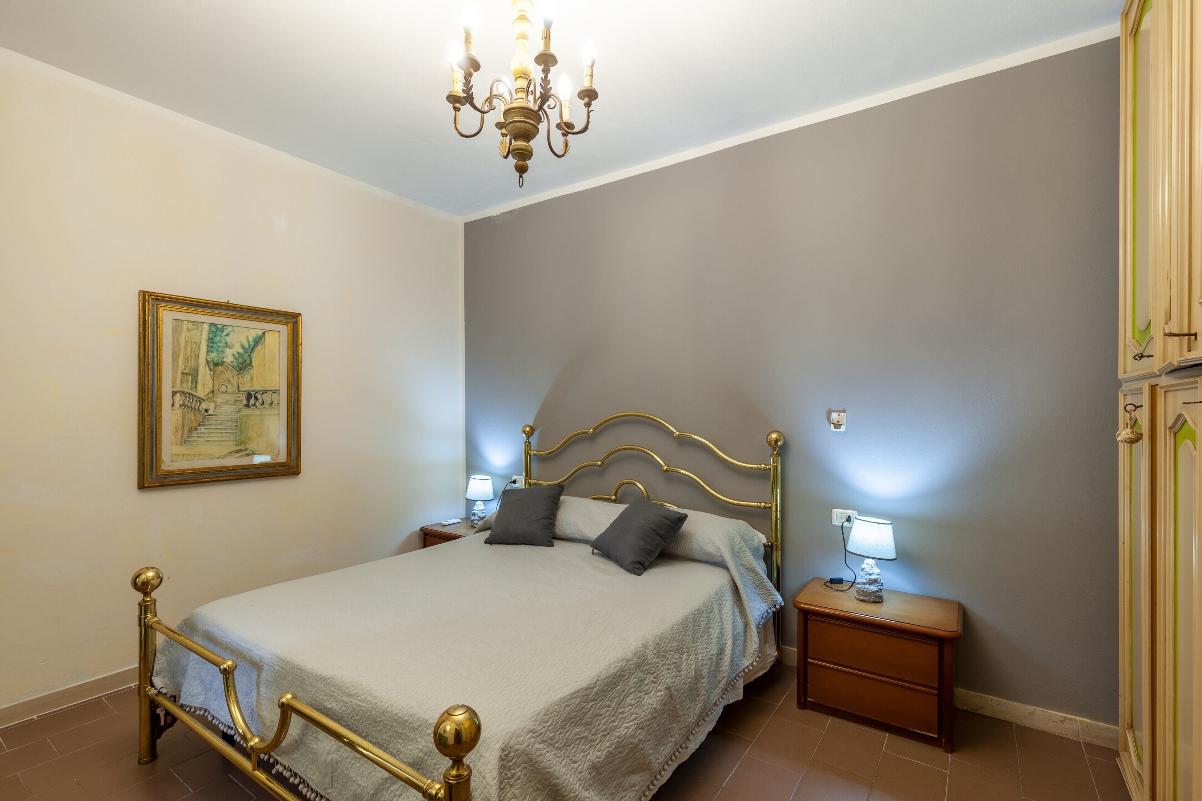 Ein Schlafzimmer mit Bett, Nachttischen, einer Chandelierleuchte, einem gerahmten Bild und einem Kleiderschrank.
