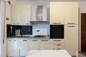 A modern kitchen with white cabinets, a black oven, a stainless steel range hood, and a marble backsplash.