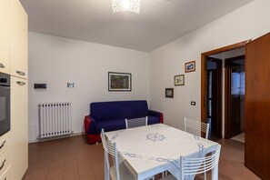 A room with a dining table, chairs, a red sofa, a white radiator, and a wooden door.