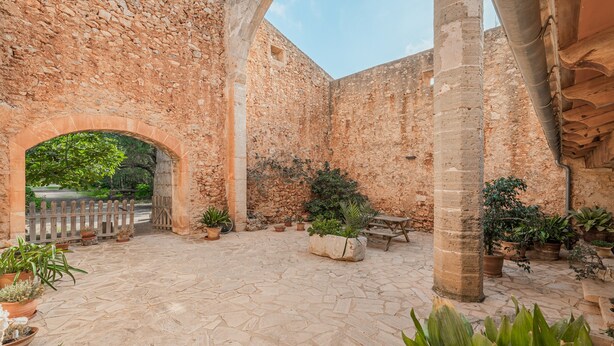 An outdoor courtyard with stone walls, a wooden bench, and potted plants. - Finca "Can Miquel des Revellar" with Mountain View, Pool & Wi-Fi (Campos)