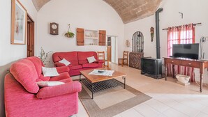 A living room with a red sofa, a wooden coffee table, a television on a wooden stand, and a fireplace. - Finca "Can Miquel des Revellar" with Mountain View, Pool & Wi-Fi (Campos)