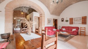A spacious living area with a wooden dining table, red sofas, and a brick archway. - Finca "Can Miquel des Revellar" with Mountain View, Pool & Wi-Fi (Campos)