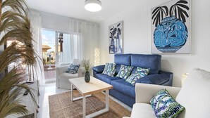 Un salón con sofá azul, sillones blancos, una mesa de centro de madera y un ventanal grande.