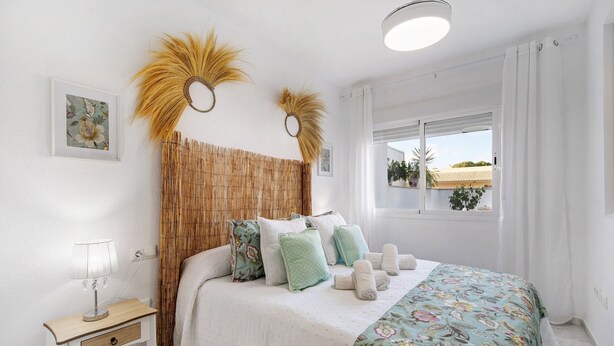Un dormitorio con cama, mesita de noche, lámpara y ventana con cortinas.