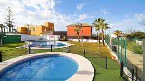 Una piscina con una valla alrededor, césped verde y edificios al fondo.