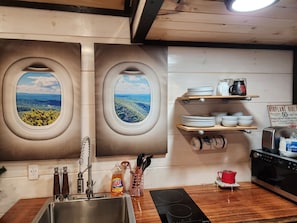 A kitchen with two windows offering views of a forested landscape, a sink with modern faucets, and a countertop with a coffee maker and a toaster.