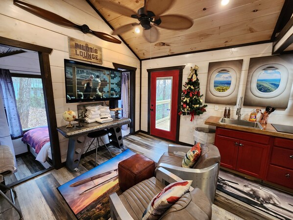 A cozy lounge area with a wooden ceiling, a red door, and a TV screen displaying a boxing match.