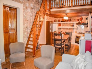 A living room with two armchairs, a sofa, a wooden staircase, and a kitchen area with a dining table and chairs. - Vacation Home "Lletreres" with Private Terraces, Private Pool & Wi-Fi (Llubi)