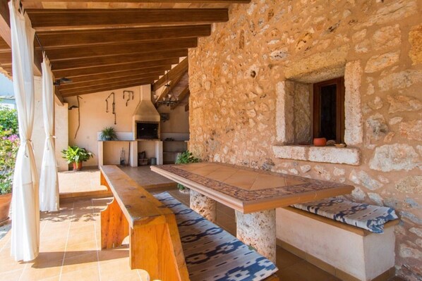 An outdoor patio with a long wooden table, stone walls, and a small window. - Vacation Home "Lletreres" with Private Terraces, Private Pool & Wi-Fi (Llubi)