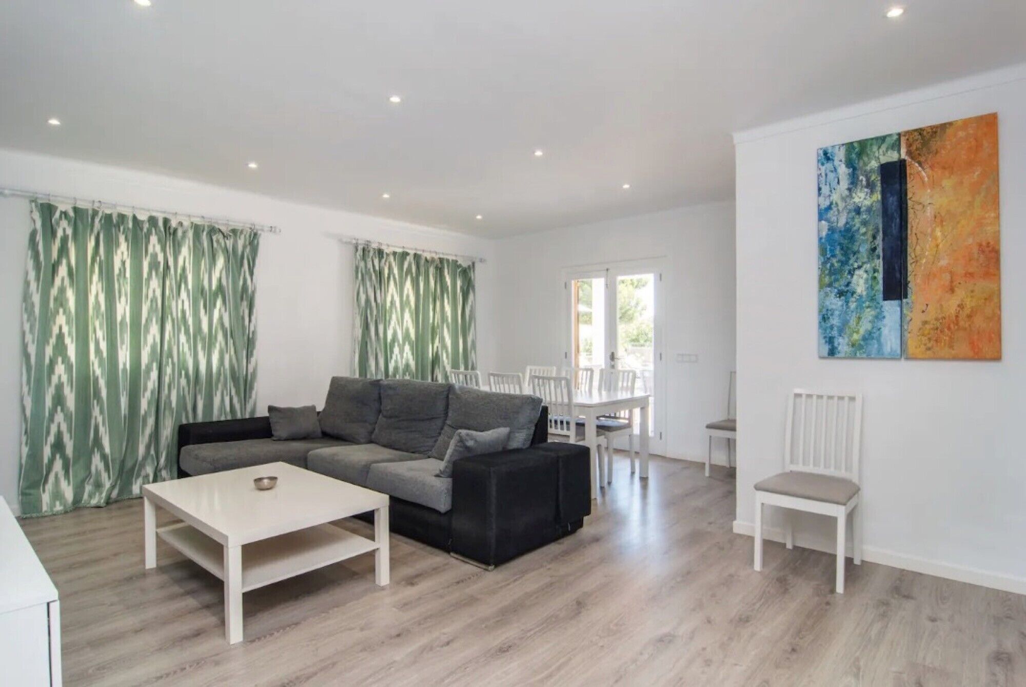 A modern living room with a grey sofa, a white coffee table, and a dining area with white chairs.