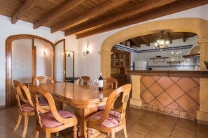 A dining area with a wooden table and chairs, a kitchen with a tiled backsplash, and a wooden ceiling.