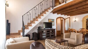 A living room with a staircase, a television, a sofa, a patterned ottoman, and a wooden ceiling. - Vacation Home "Tirasset" with Private Pool, 2 Terraces & Wi-Fi (Llubi)