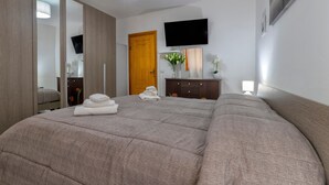 Un dormitorio con una cama grande, un armario, un televisor montado en la pared y una puerta.