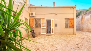 Un edificio con un patio adoquinado, una motocicleta estacionada afuera y una puerta que da a una habitación.