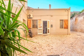 A building with a cobblestone courtyard, a motorcycle parked outside, and a door leading to a room.