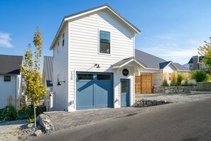 Une maison à deux étages avec une porte de garage bleue, un mur en pierre et un petit arbre dans le jardin.