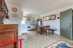 A kitchen with a dining table, chairs, and a red chair. There is a wooden cabinet, a stove, and a refrigerator.