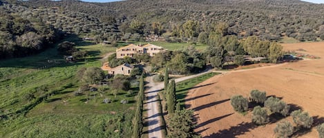 A large stone house with multiple rooms, surrounded by a well-maintained garden and a dirt path leading to the entrance.