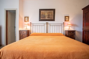 A bedroom with a bed, two bedside tables, a nightstand, a door, and two wall-mounted lamps.