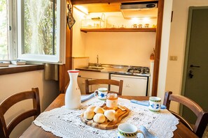 Una mesa de comedor con mantel de encaje blanco, una tabla de madera con panecillos, una jarra blanca, un tarro de miel y dos tazas de café con un diseño azul.