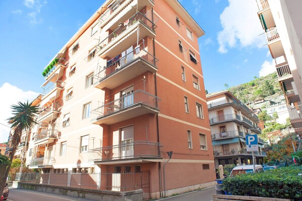 A multi-story residential building with balconies, a parking sign, and a clear sky.