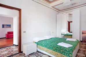 A bedroom with a bed, a nightstand, a red chair, and a mirror.