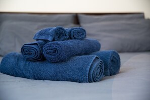 Una cama con toallas azules enrolladas y almohadas grises.