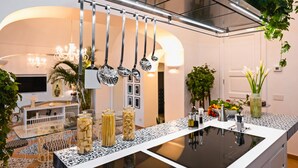 A modern kitchen with hanging utensils, a glass-top dining table, and a built-in stove. - AMORE RENTALS - Villa Mare Blu with Internal Heated Pool, Sea View and Breakfast (Praiano)