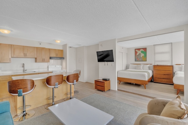 A modern hotel room with a kitchenette, a bed, a TV, and a sofa. - Deluxe Waikiki Condo Pool View FREE Parking & Wi-Fi (Honolulu)