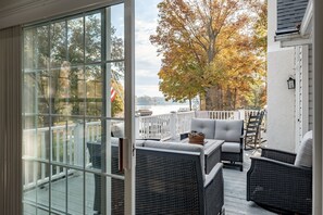 A covered outdoor deck with wicker furniture, a white railing, and a view of trees and water.