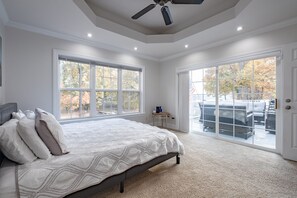 Quarto com uma cama grande, duas janelas, ventilador de teto e vista para móveis de exterior.
