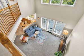 Un vaste espace de vie agrémenté d’un tapis gris, d’un canapé bleu, d’une table basse ronde et d’un escalier en bois.