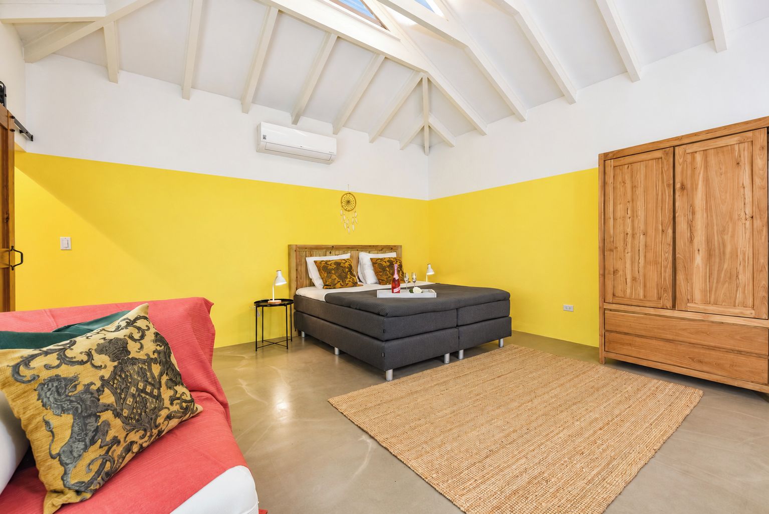A bedroom with a bed, a wardrobe, a bedside table, and a red sofa.