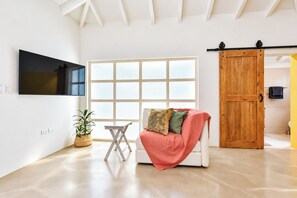 Ein modernes Wohnzimmer mit einem weißen Sofa, einem kleinen Tisch, einem Blumentopf und einem großen Fenster.