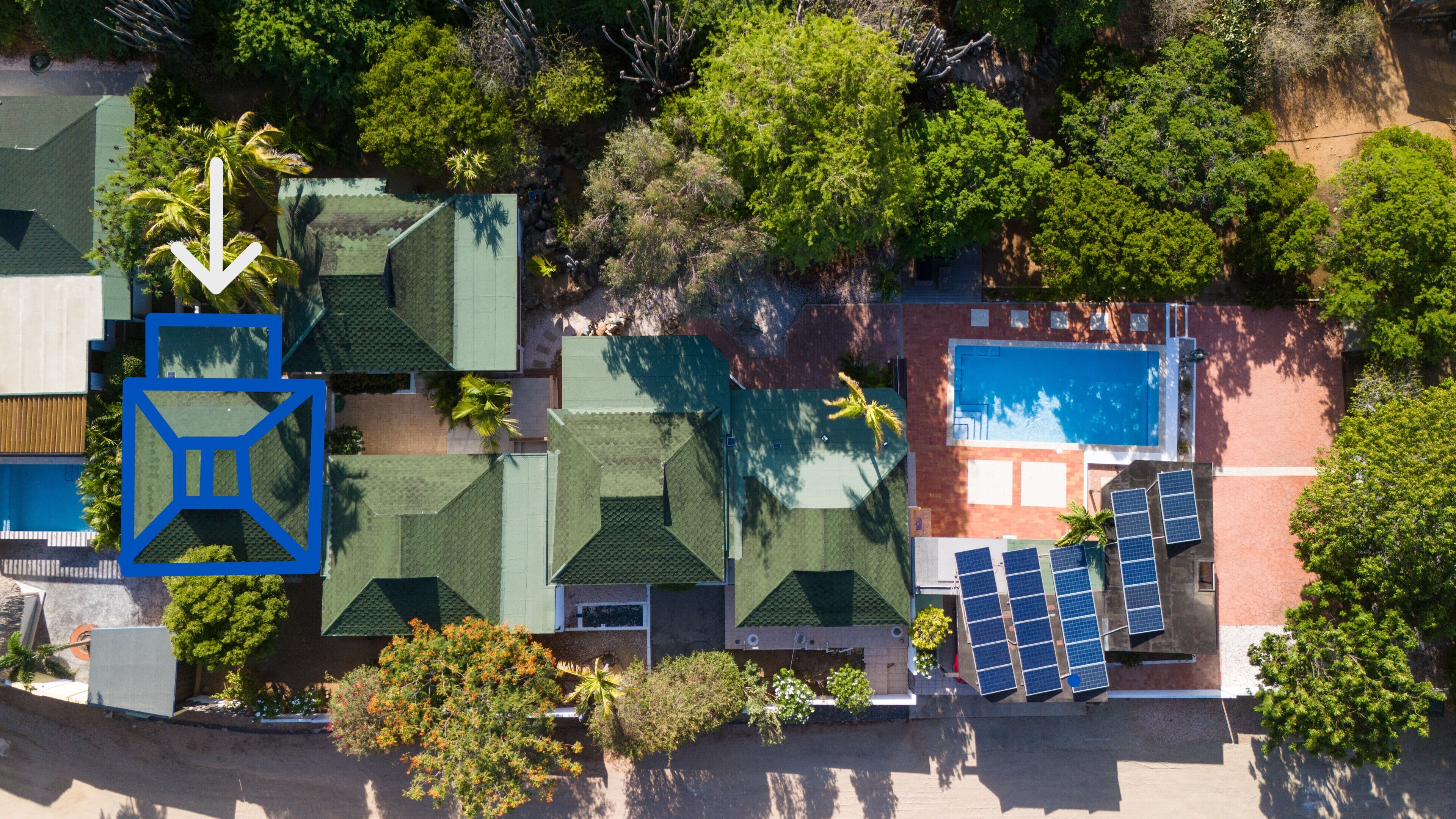 Vue aérienne d’un complexe hôtelier doté d’une piscine, de chaises longues et d’une grande variété d’arbres et de plantes.