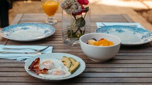 A breakfast table set outdoors with plates, bowls, and a glass of orange juice. - Hotel Boutique Can Pocovi (Sant Llorenc des Cardassar)