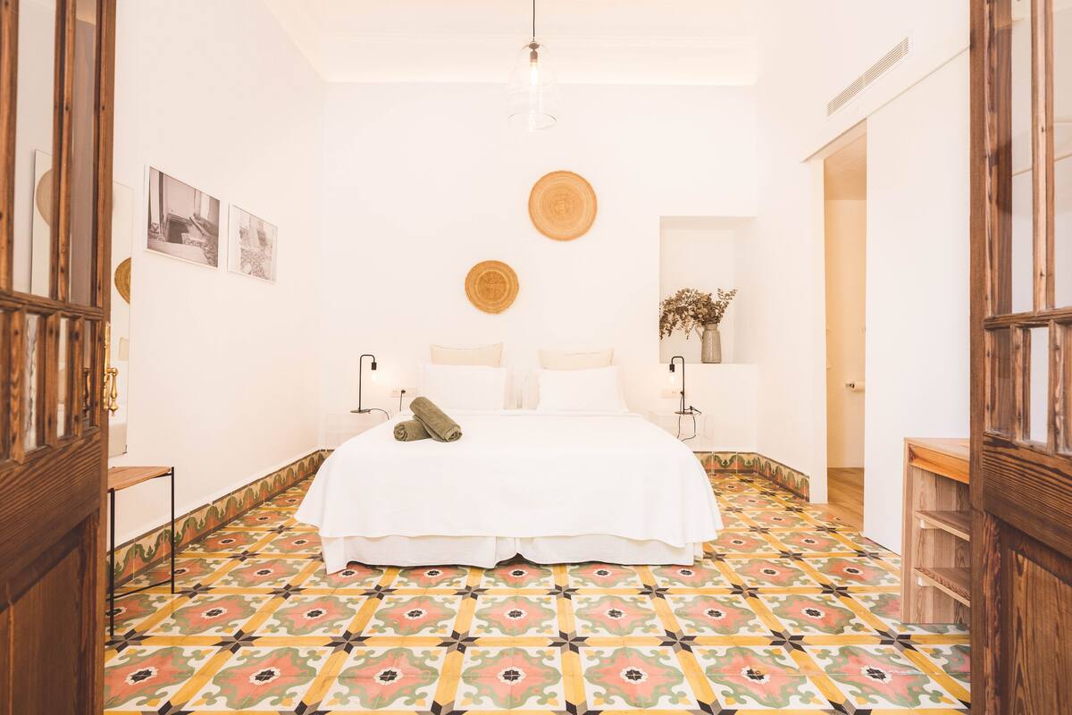 Een slaapkamer met een bed, een nachtkastje, een plank aan de muur met een plant, en een vloer met patroon.