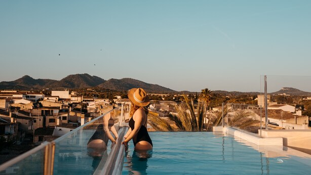 A woman in a swimsuit and hat by a pool with a view of a town and mountains. - Hotel Boutique Can Pocovi (Sant Llorenc des Cardassar)
