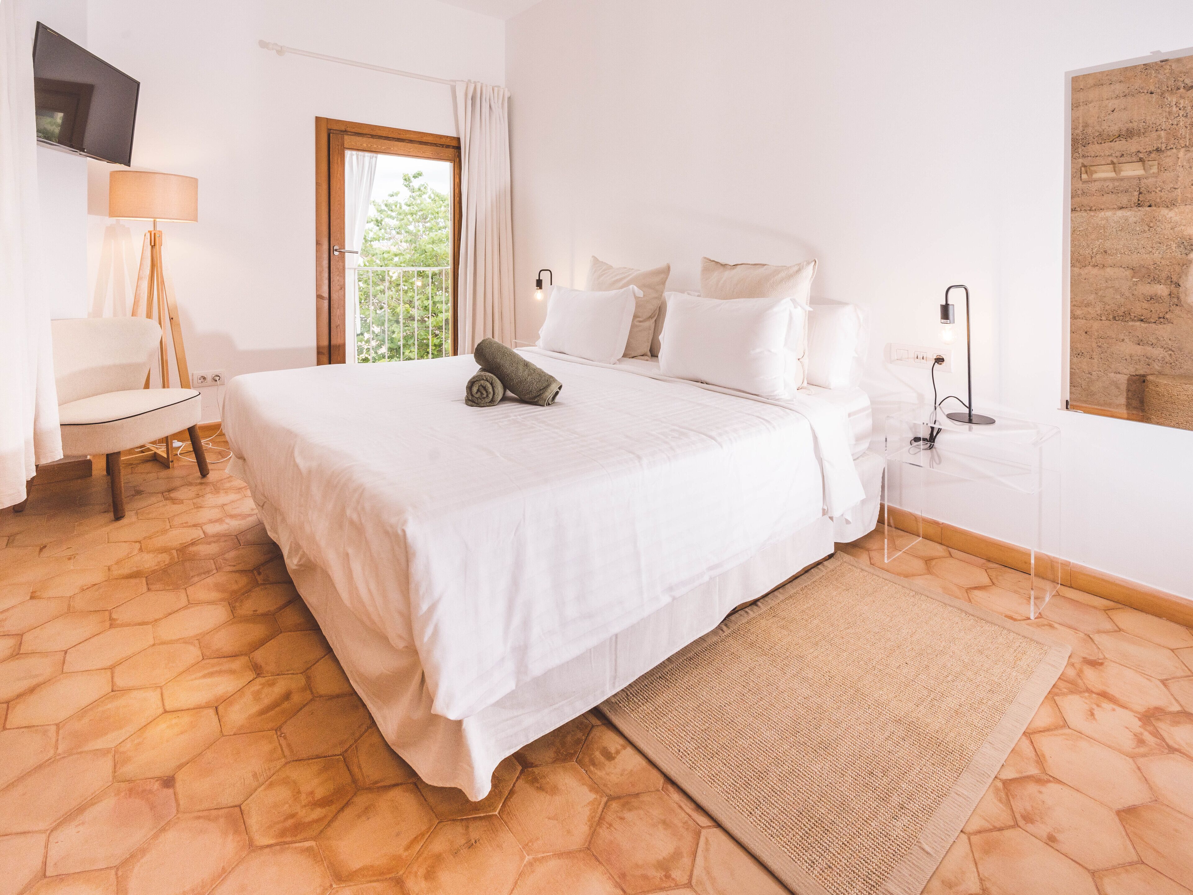 Une chambre avec un grand lit, une table de chevet, une lampe et une vue sur la verdure.