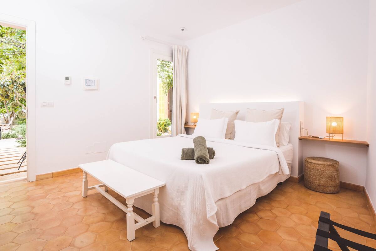 Een slaapkamer met een groot bed, een nachtkastje, een bankje, een bedlamp en uitzicht op de omgeving.