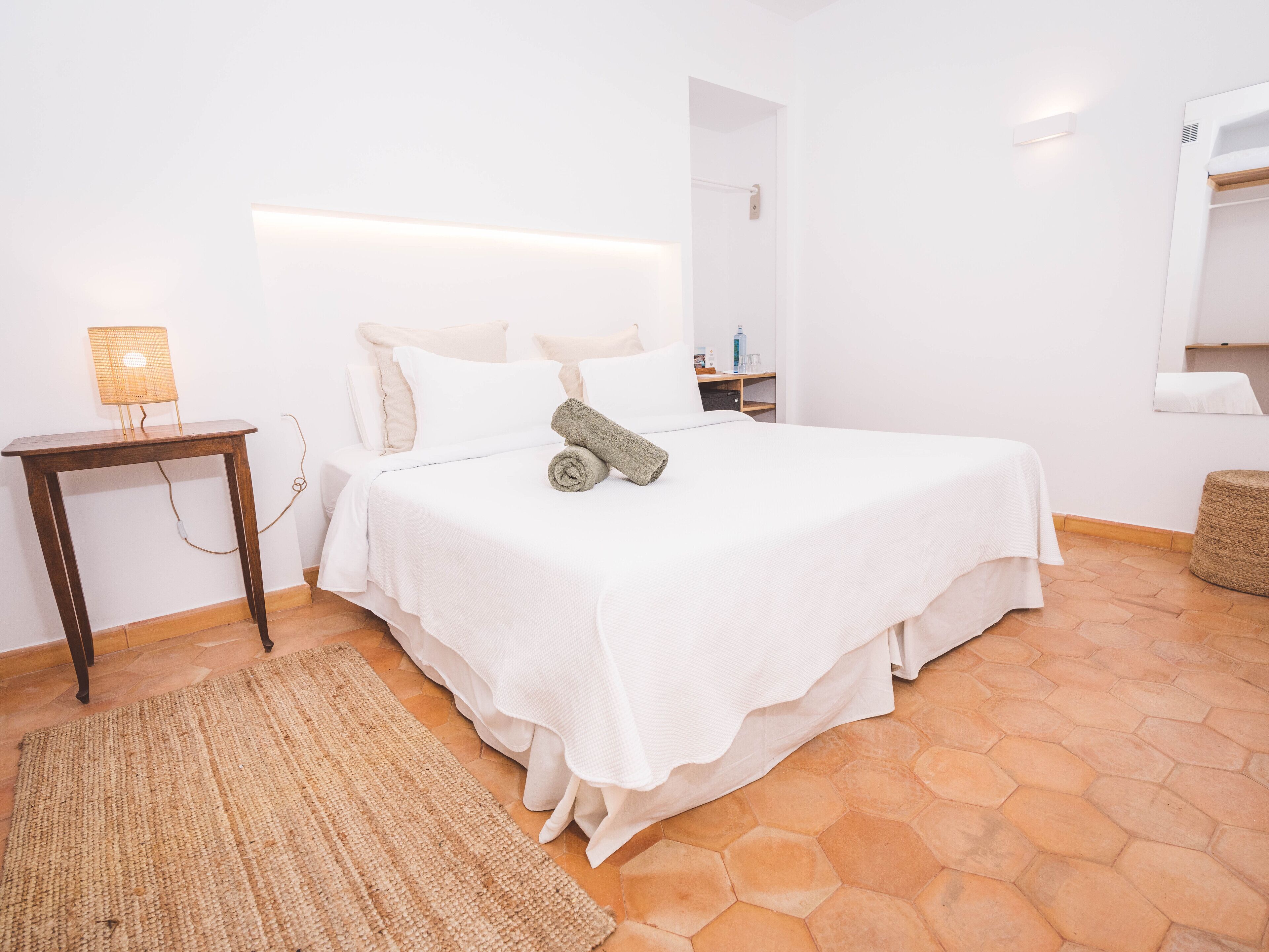 A neatly arranged bedroom with a bed, bedside table, and a mirror.