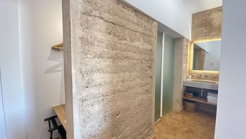 Ein Zimmer mit einer Wand aus strukturiertem Stein, einem Holzstuhl, einem Waschbecken mit Spiegel und einem Fliesenboden.