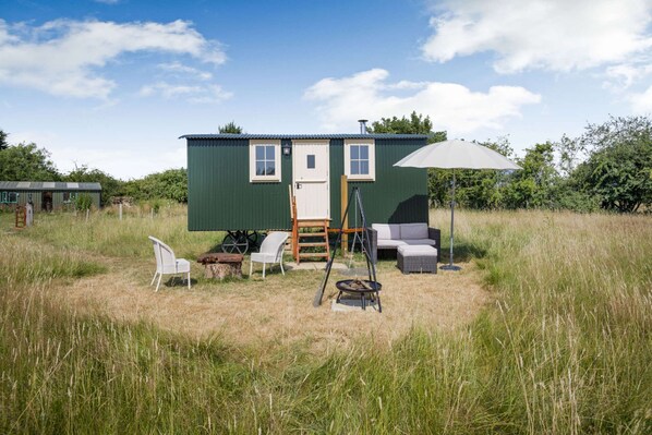 A small green house with a porch, two white chairs, a swing, and a table.