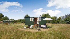 A small, green mobile home with a porch area, a swing set, and a single umbrella.