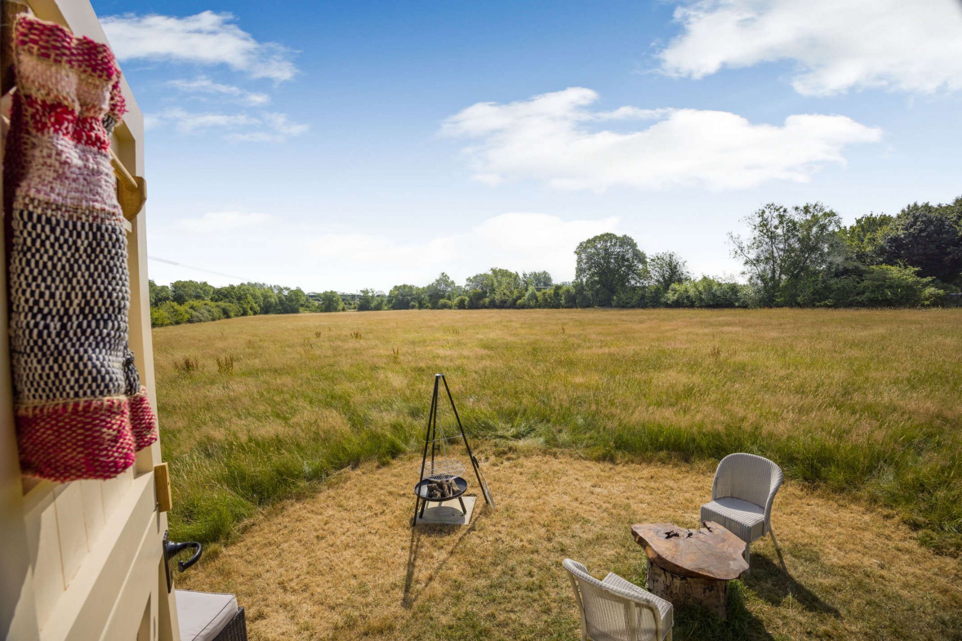 A backyard with a grassy field, a wooden swing, and a wicker chair.