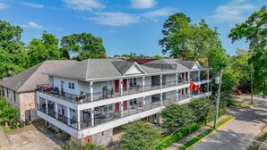 A two-story building with a balcony on the ground floor, a red door, and a flag. - Crimson Court - Book Now for Football! (Tuscaloosa)
