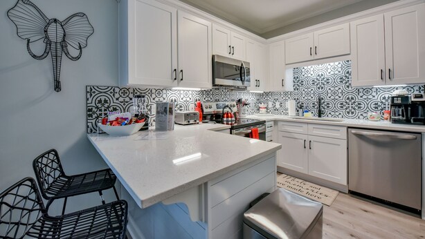 A modern kitchen with white cabinets, a stainless steel dishwasher, and a patterned backsplash. - Crimson Court - Book Now for Football! (Tuscaloosa)
