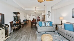 Uma sala de estar espaçosa com um sofá cinzento, uma mesa de centro e um espaço de refeições com mesa e cadeiras.
